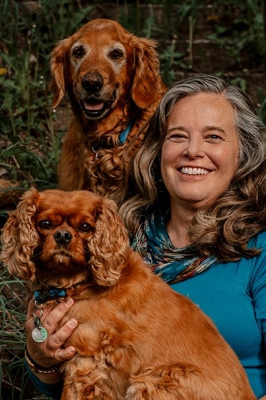 Jen VonLintel smiling with her two dogs, a golden retriever and spaniel.