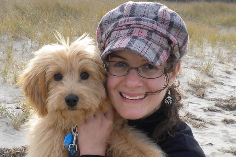 woman in hat holding small dog and smiling. 