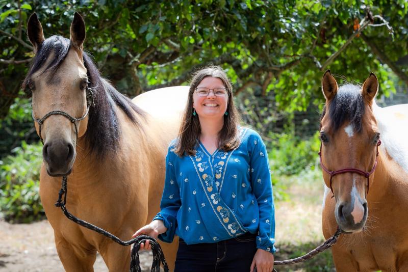 woman smiling and standing between two horses at a therapeutic ranch
