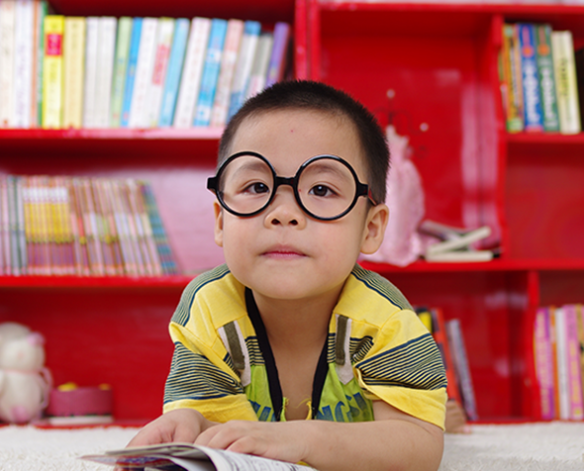 small boy in library reading a book​
