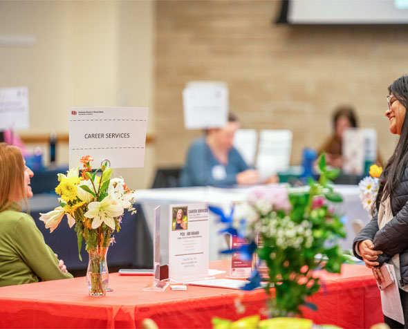 Student standing in front of a table with a sign reading Career Services getting information from a DU representative