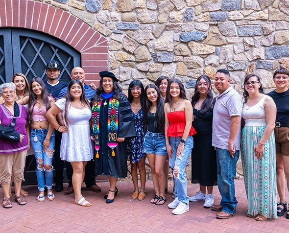 PhD grad Xochilt Alamillo dressed in regalia with family and friends during PhD hooding ceremony