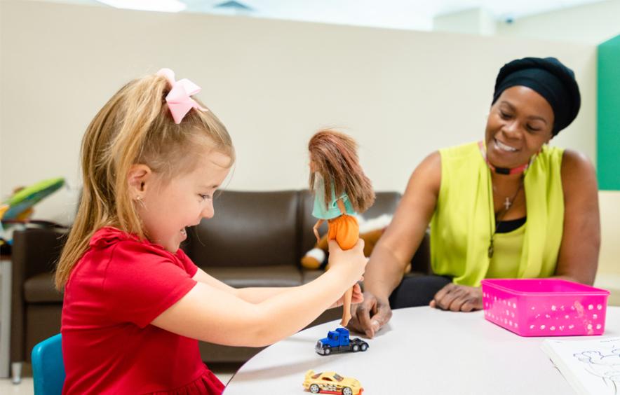 Child playing with doll, woman watching