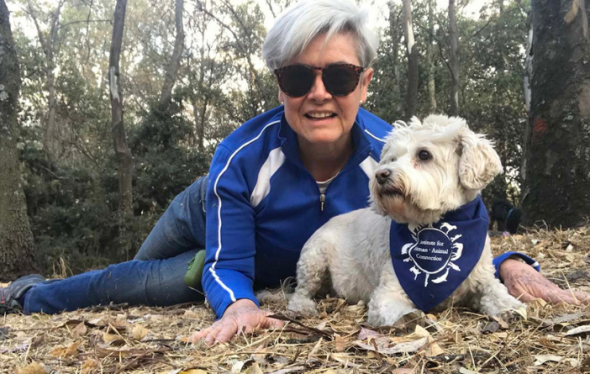 Woman on the ground near small white dog wearing an IHAC bandana