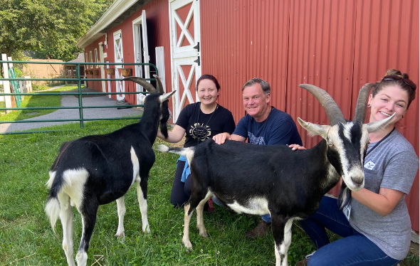 Three people with two goats standing outside