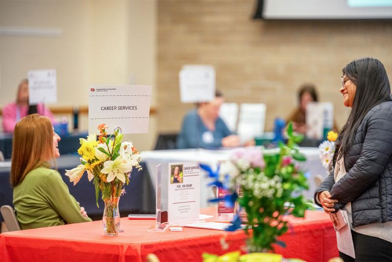 Student standing in front of a table with a sign reading Career Services getting information from a DU representative