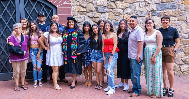 PhD grad Xochilt Alamillo dressed in regalia with family and friends during PhD hooding ceremony