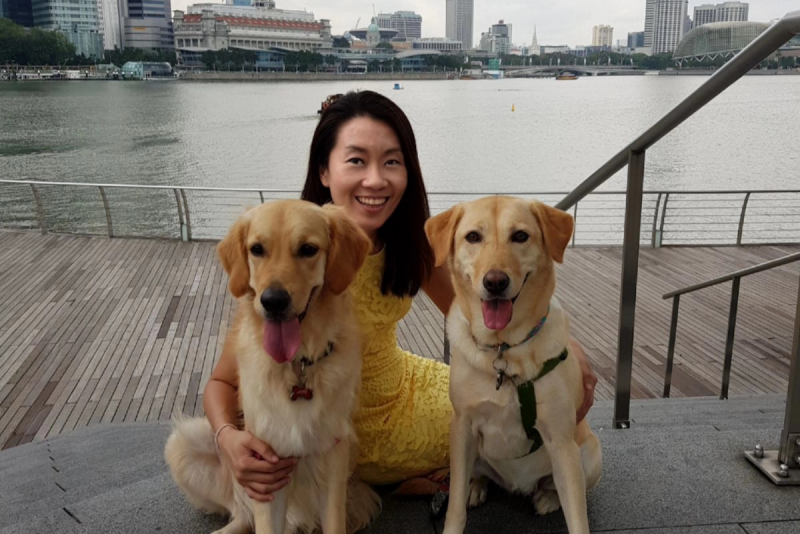 Maureen Huang, a woman with long dark hair, poses with a her dogs near an urban harbor