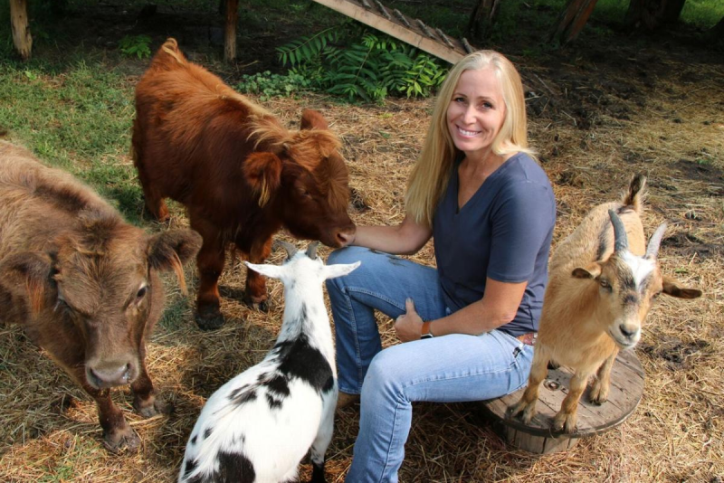 Pamela Wheeler seated outside surrounded by goats and calves.