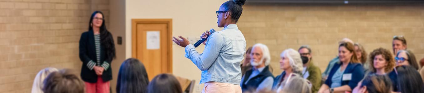 woman standing up asking a question at a community event in Craig Hall