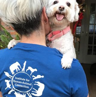 woman holding a small white dog with the Institute for Human-Animal Connection logo on her shirt