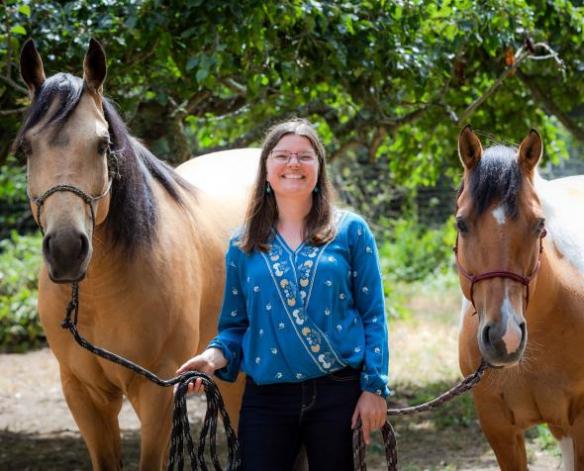 woman smiling and standing between two horses at a therapeutic ranch